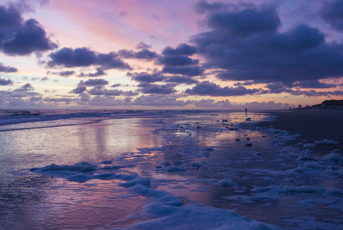 Ein farbenfroher Sonnenuntergang am Meeresufer. Die Farben reichen von lila bis gelb und werden teilweise von schönen Wolken verdeckt.
