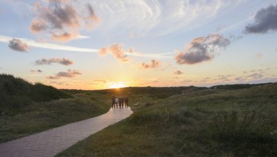 Eine Wandertruppe läuft durch die Dünen von Langeoog in Richtung Sonnenuntergang