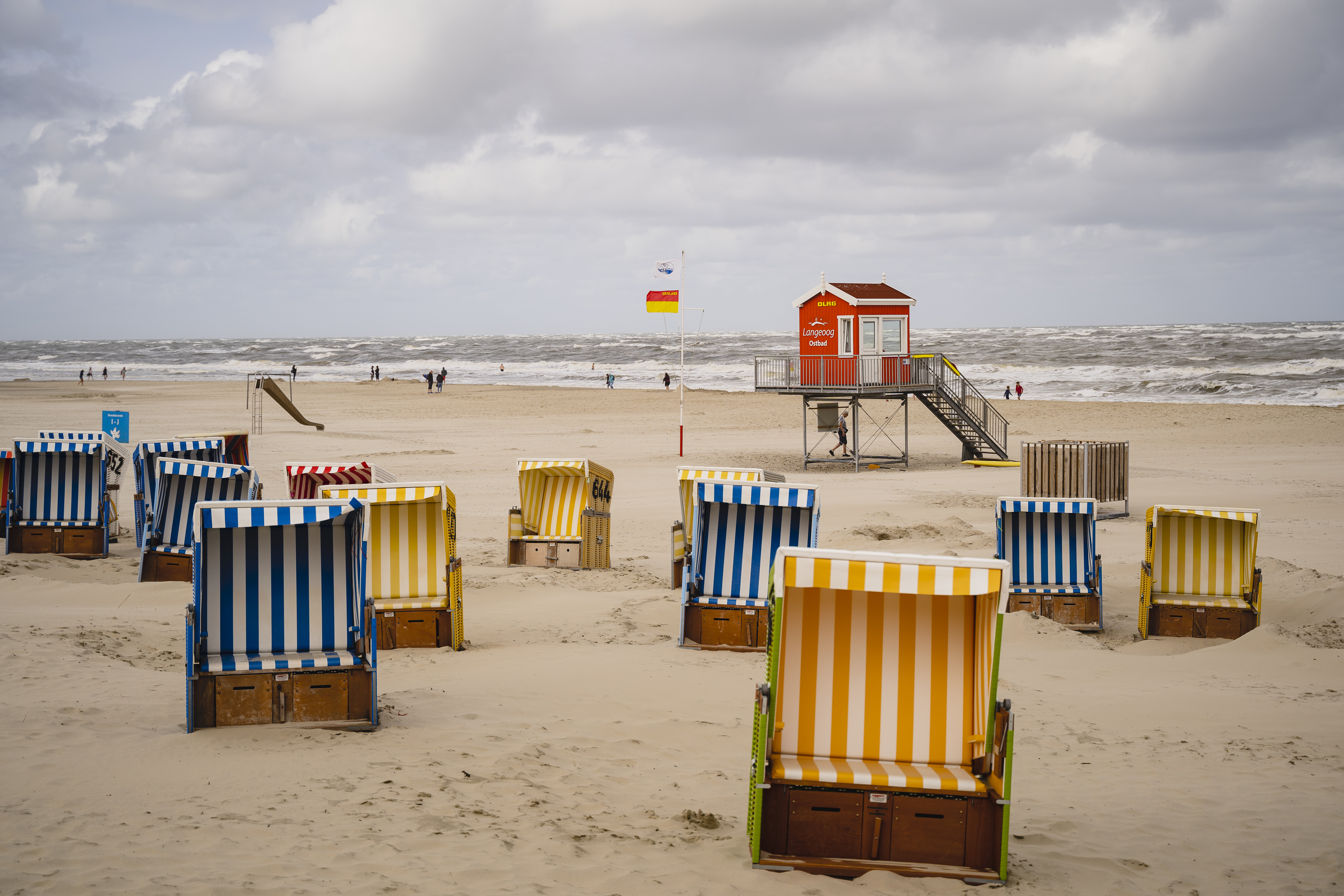 Sehr viele Strandkörbe in den Farben rot, gelb und blau stehen vor dem Strandhäuschen der DLRG am Langeooger Strand